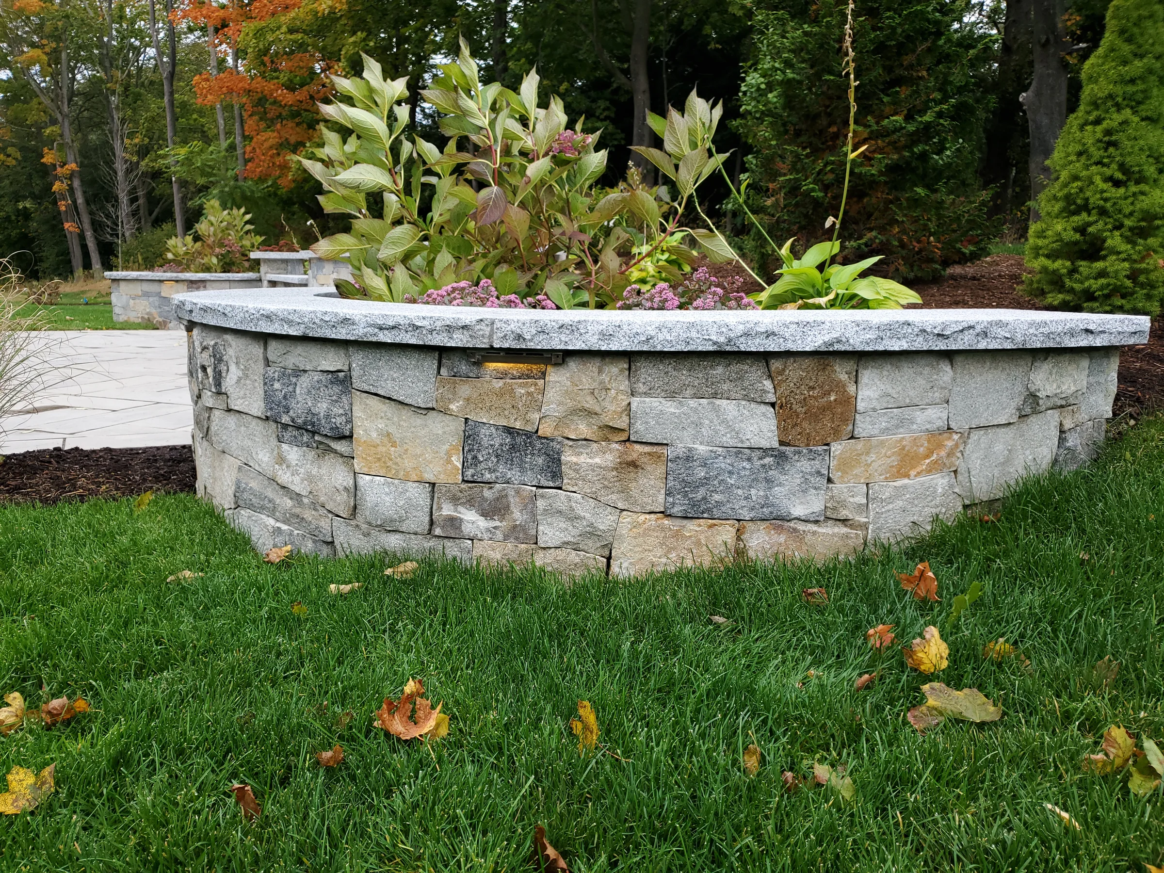 Curved stone planter with a granite cap and mixed planting