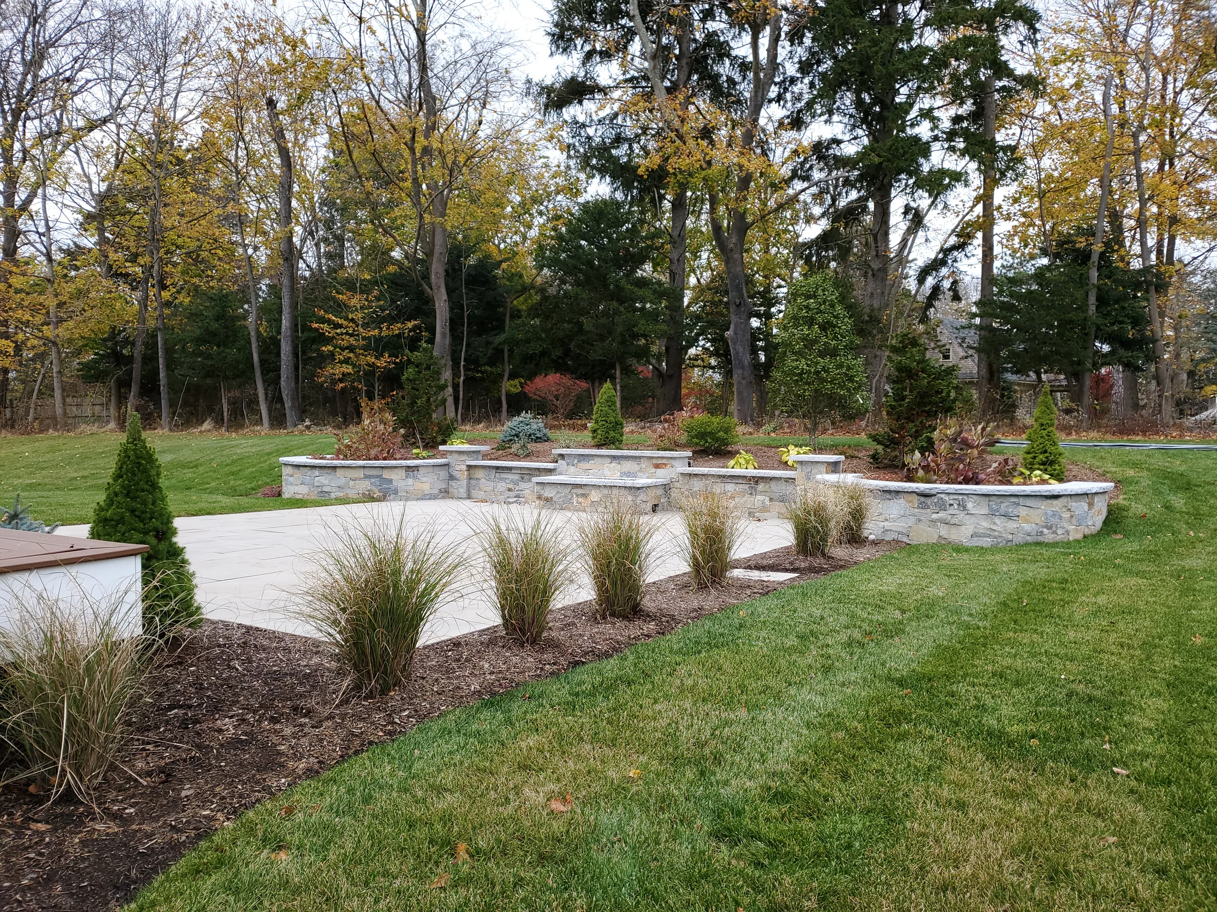 Back lawn with a low stone wall and paved outdoor area