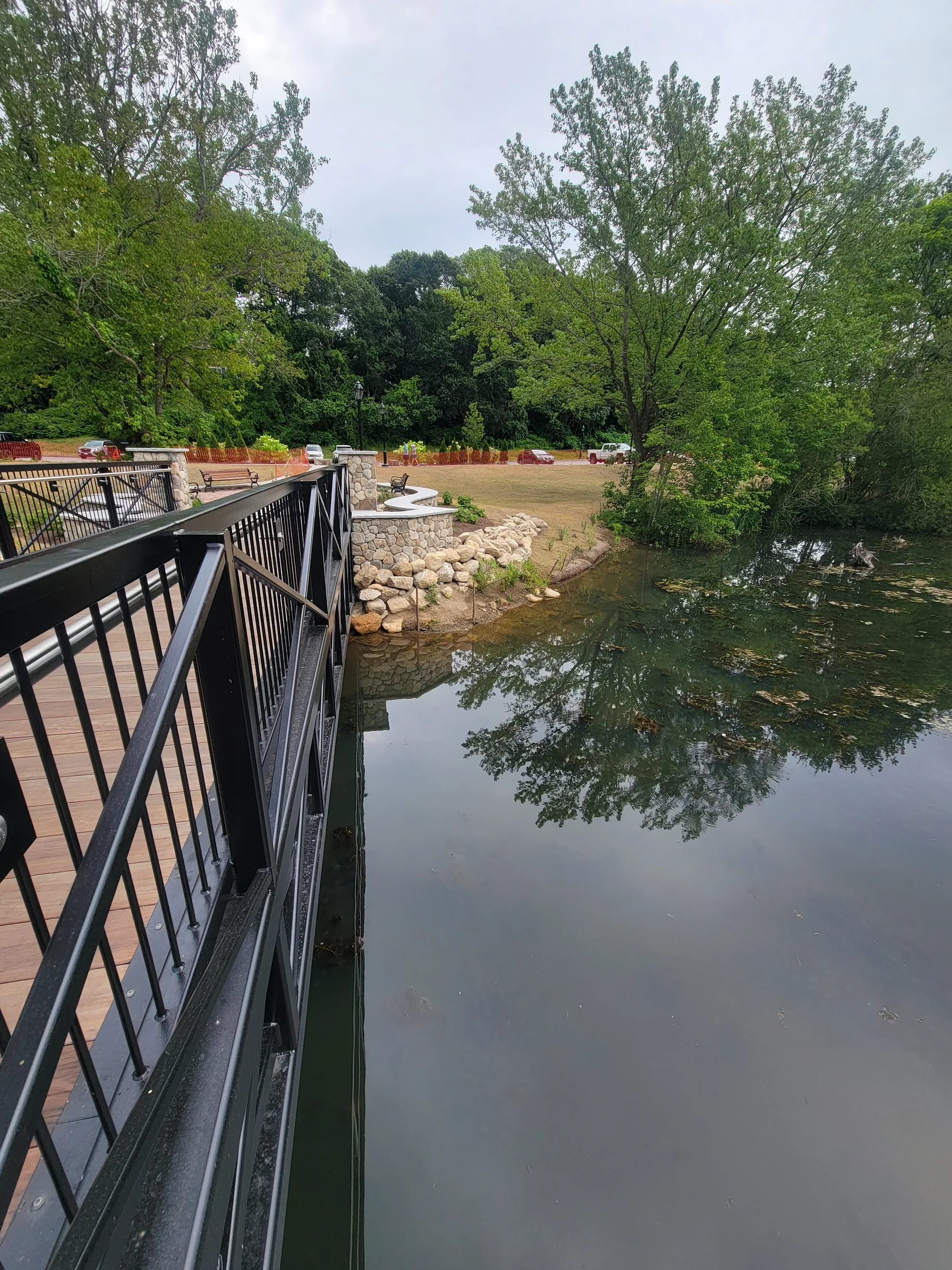 View from a black-railed footbridge across a pond toward a stone-edged terrace