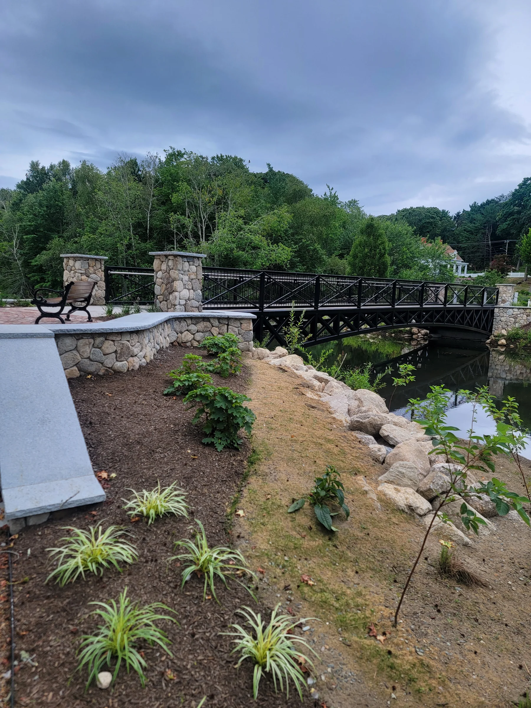 Pond-edge planting bed and stone border beside a footbridge