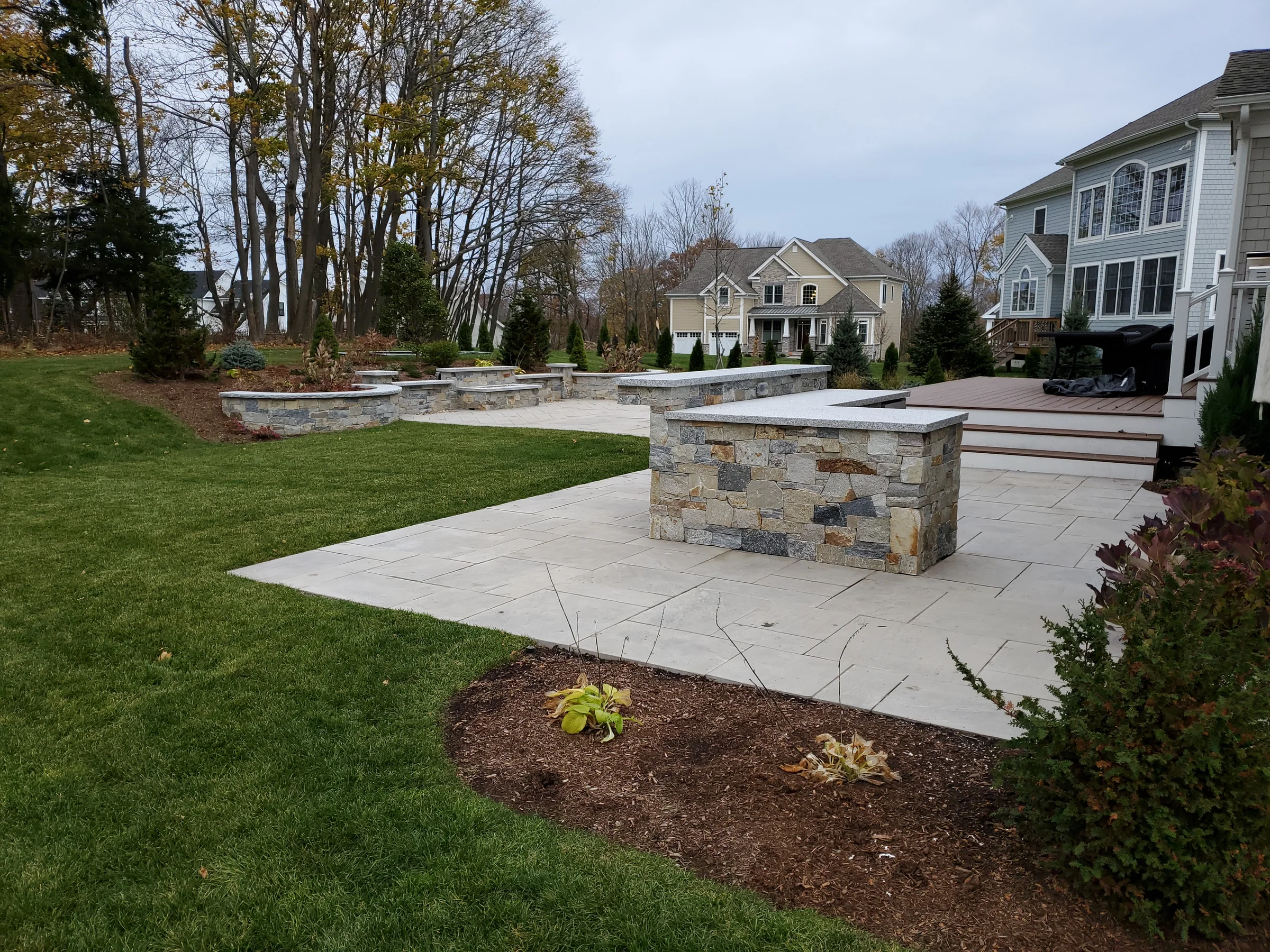 Stone patio with a low wall, planting beds and nearby deck