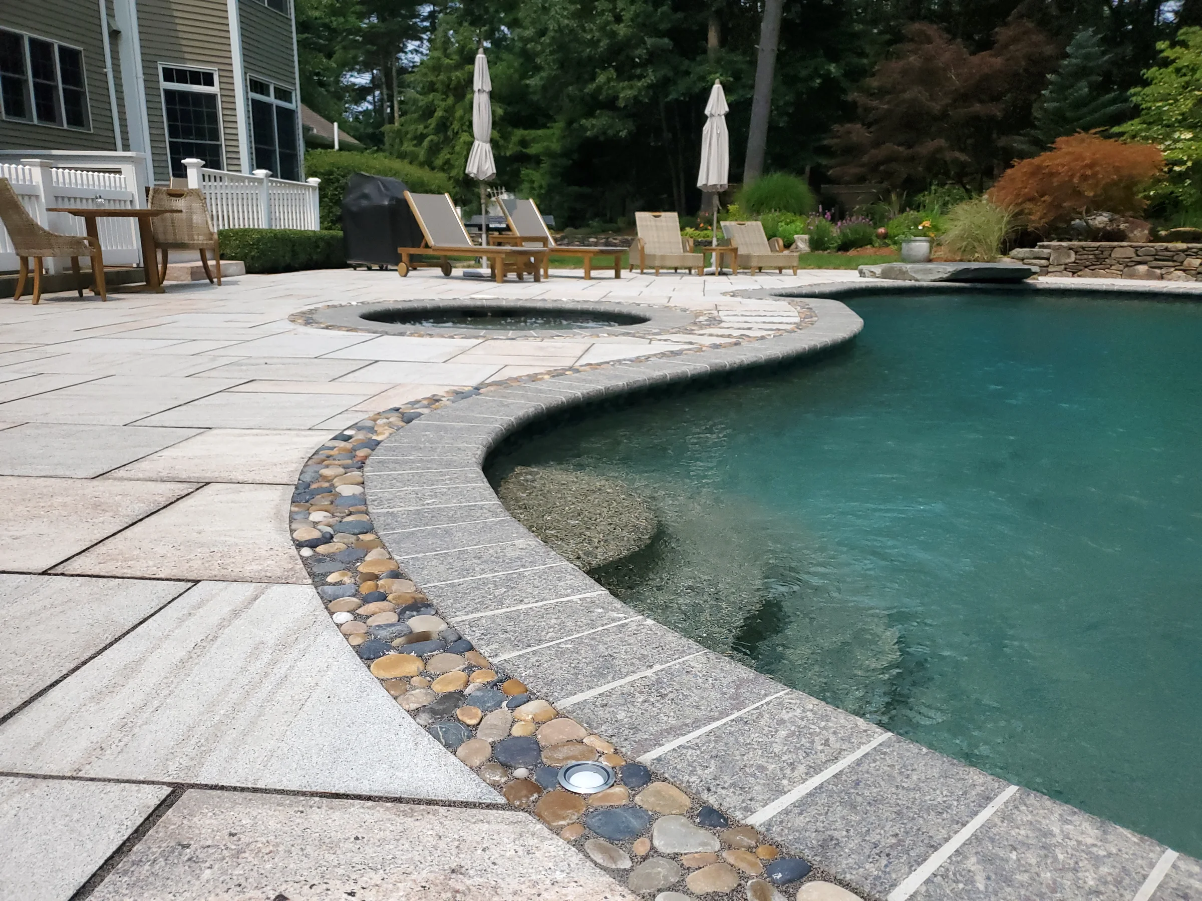 Close view of a curved pool edge with stone coping and pebble detail