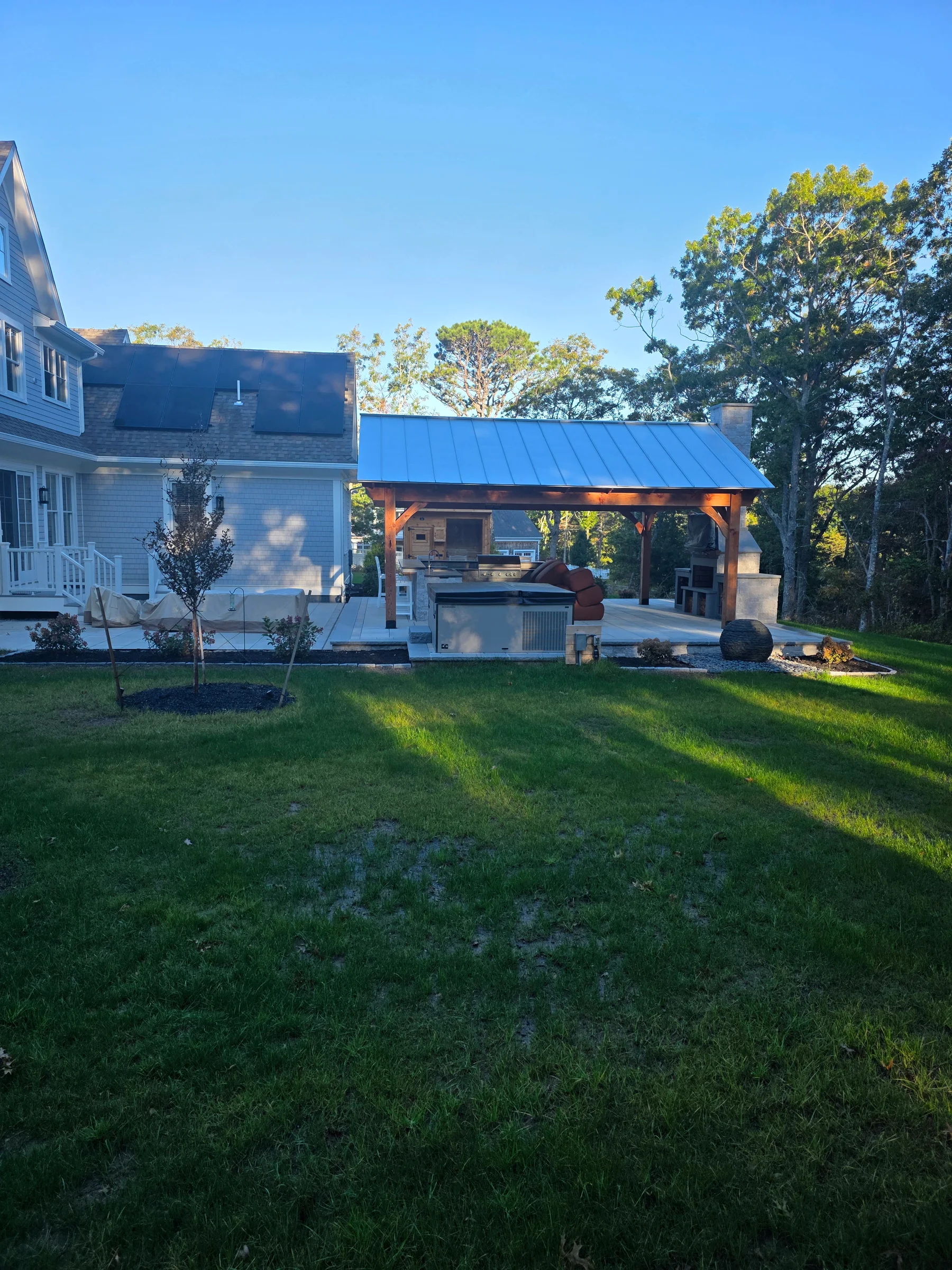 Timber pavilion and outdoor kitchen beside a gray-shingled home