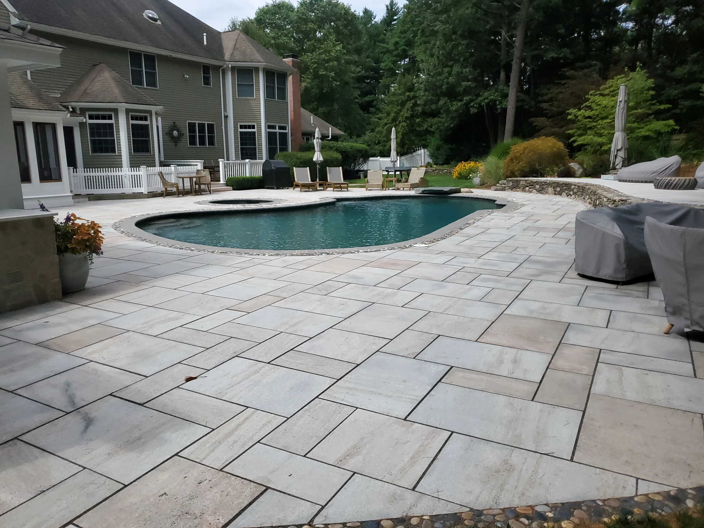Curved swimming pool surrounded by a broad pale stone patio