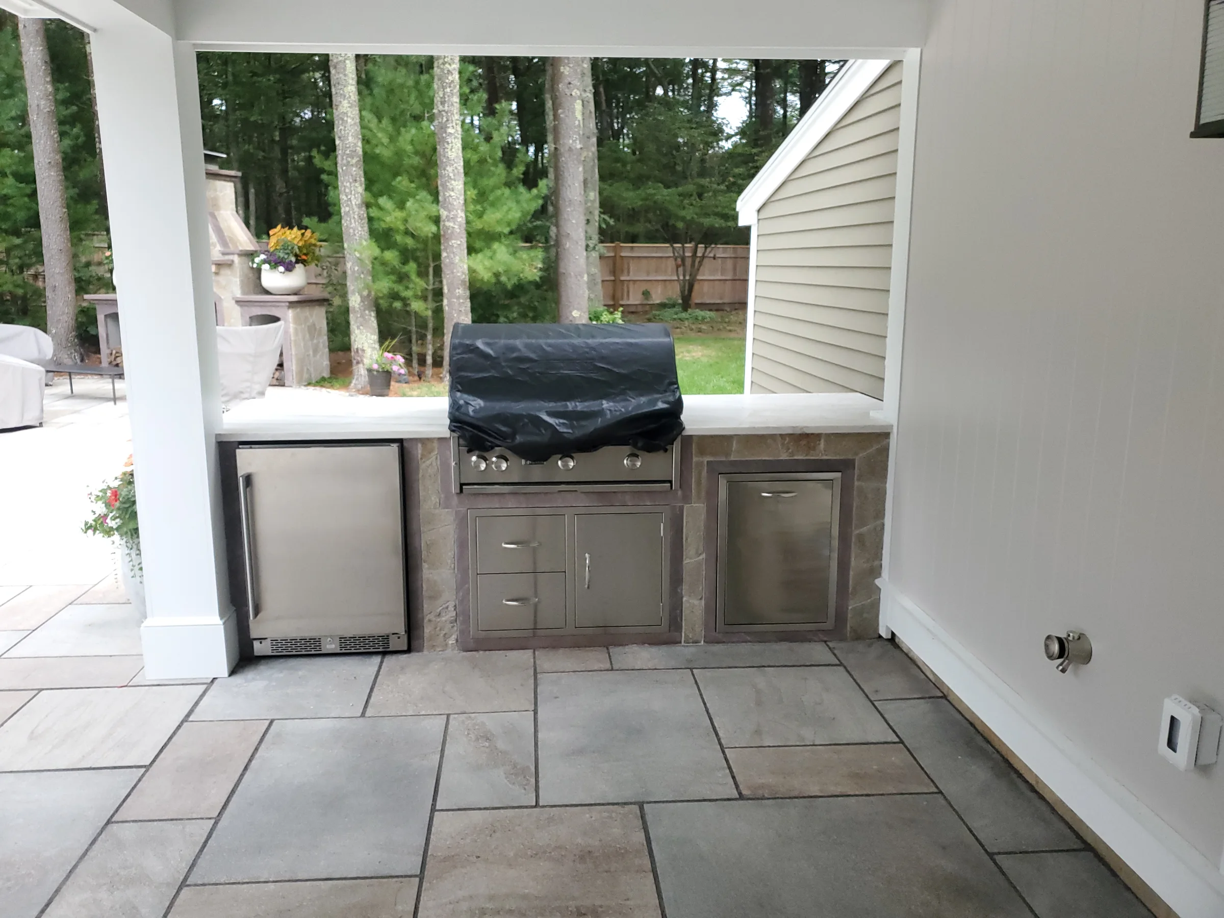 Covered outdoor kitchen with a built-in grill and stone floor